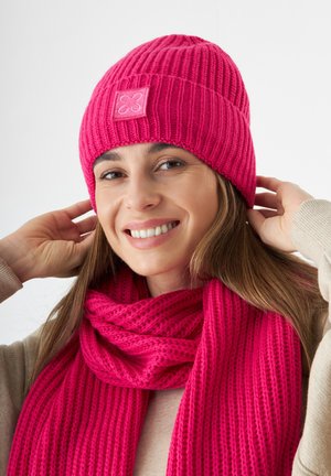 Pink knitted beanie with a textured ribbed pattern and small logo patch; matching pink knitted scarf with similar ribbing detail.