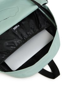 Mintgrön ryggsäck med svart insida, dragkedjestängning och vadderat fack för en laptop. Har VANS-logotyp inuti.
