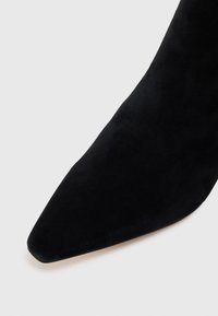 Botine din suede negre, cu vârful ascuțit și textură fină. Prezintă un profil elegant, punând accent pe designul minimalist.