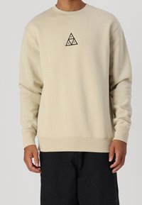 Felpa beige in misto cotone con scollo rotondo, maniche lunghe e un piccolo logo triangolare nero sul petto.