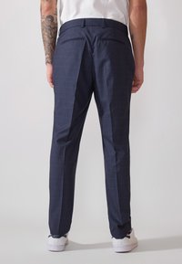 Pantalons de costume à carreaux marins avec une coupe ajustée, dotés de deux poches arrière et d'un pli sur le devant des jambes, assortis à des baskets blanches.