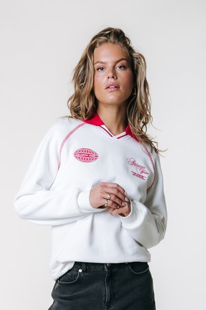 Hanorac alb cu guler roșu; prezintă logo-uri și accente roșii brodate; croială lejeră cu manșete rib; textură moale.