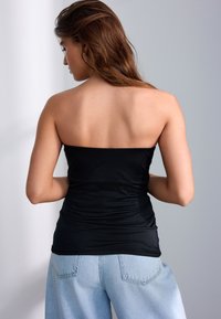 Sort stropløs top med rynket tekstur, parret med lyseblå jeans med høj talje, der fremhæver en glat og tilpasset silhuet.