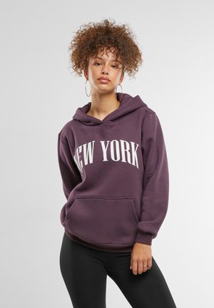 Lila kapucnis pulóver, fehér "NEW YORK" felirattal. Kangúzsebes, állítható húzózsinóros kapucnival és laza fazonnal rendelkezik. Fekete leggingsszel párosítva.