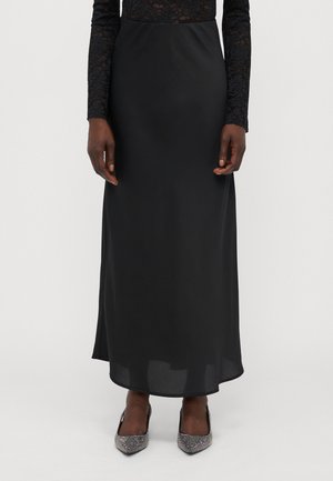 Schwarzer Satin-Midirock mit glatter Textur, geradem Schnitt und subtiler Glanz, kombiniert mit silbernen, verzierten spitzen Pumps.