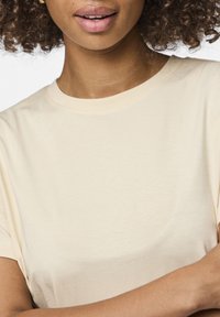 Crew-neck, kortermet t-skjorte i lys beige stoff, med en myk tekstur og minimale sømdetaljer.