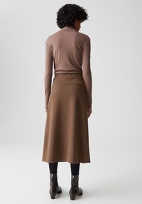 Maglietta marrone a maniche lunghe abbinata a una gonna maxi marrone, completata da leggings neri e stivaletti con cerniere argentate.