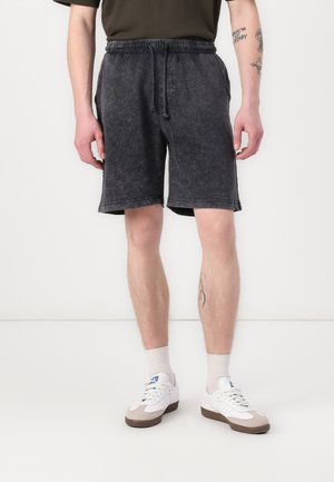 Shorts noirs avec texture, taille élastique et cordon de serrage, dotés de poches latérales et d'une coupe décontractée, associés à des baskets blanches.