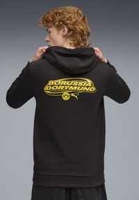 Sort hættetrøje lavet af en bomuldsblanding, med et stort gult "Borussia Dortmund" logo på ryggen, samt en kængurulomme og ribbede manchetter.