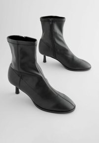 Black leather ankle boots with a pointed toe, zip closure, and a small heel. Features stitched detailing along the upper seam.