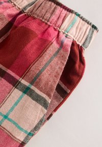 Punainen ja vaaleanpunainen ruudullinen kangas, jossa erilaisia kuvioita, kuminauhavyötäröllä ja teksturoidulla pinnalla. Korostuksia teemansinisissä ja ruskeissa raidoissa.