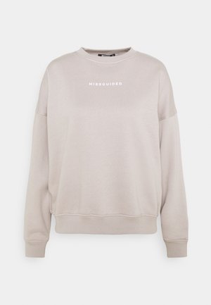 Beige väpytakki pitkillä hihoilla, jossa "MISSGUIDED"-logo valkoisella tekstillä rinnan keskellä.