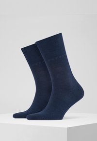 Calze di cotone blu navy con una texture a costine e un logo discreto. Hanno una lunghezza a metà polpaccio e una forma standard della punta.