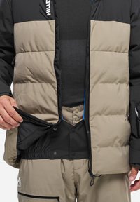 Wattierte Jacke in Schwarz und Beige mit einem Reißverschluss vorne, elastischem Bund und einer Innentasche. Das Material ist weich und strukturiert.