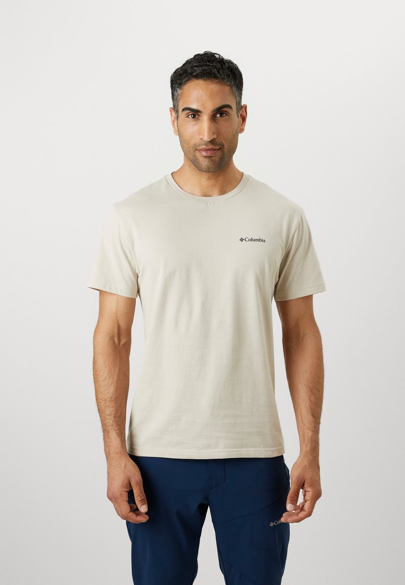 T-shirt en coton beige avec col rond et manches courtes. Présente un petit logo noir sur la poitrine gauche. Texture lisse, coupe décontractée.