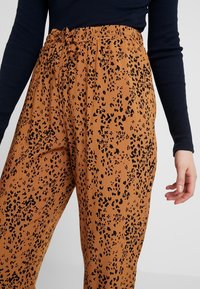 Hnědé kalhoty s leopardím vzorem, které mají elastický pas a šňůrku na stažení. Materiál vypadá jemně a má lehký textil, se černými skvrnami.