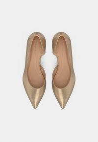 Χρυσά δερμάτινα παπούτσια μπαλαρίνας με μυτερή μύτη και υφή, με σχεδιασμό slip-on και απαλή εσωτερική επένδυση. Το όνομα της μάρκας είναι ορατό στο εσωτερικό.