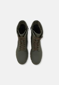 Bottes imperméables vert olive à tiges hautes, à lacets et fermeture éclair latérale. Texture lisse et semelle en caoutchouc antidérapante.