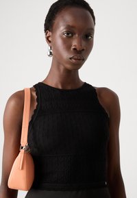 Top nero in maglia con motivo tessurizzato e bordi scallop, abbinato a una borsa color pesco con forma strutturata e hardware argentato.