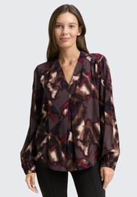 Long-sleeve blouse in dark maroon with an abstract pattern of cream, purple, and brown. Features a V-neck and gathered cuffs. Soft fabric.