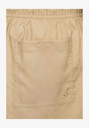 Beige kangas jonka pinta on sujuva, jossa on joustava vyötärö ja suuri läppätasku takana näkyvin tikkauskoristein.