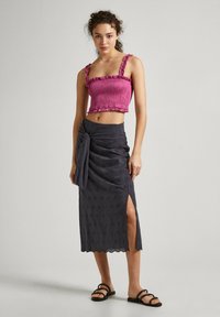 Top corto fucsia con tirantes con volantes, combinado con una falda gris oscuro que presenta una abertura lateral y un patrón floral bordado.