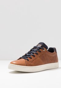 Braune Leder-Sneaker mit navyfarbenen Schnürsenkeln, einer weißen strukturierten Sohle und dezenten Stickdetails. Rundliche Zehenform und gepolsterte Ferse.