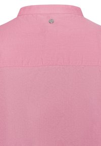 Achterkant van een roze katoen shirt met een kraag en een kleine ronde zilveren logoknoop nabij de halslijn.