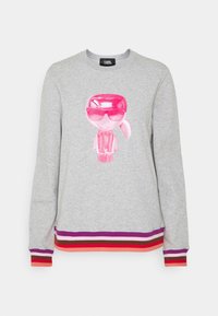 Sweat-shirt gris clair avec une figure de dessin animé rose brillante portant des lunettes de soleil à l'avant, et des poignets et un ourlet rayés multicolores violet, rouge et orange.