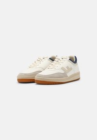 Sneakers con una toma in pelle crema e dettagli in suede beige, tallone blu navy e suola in gomma marrone. Design classico con lacci.