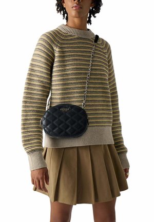 Femme portant un pull en maille rayé, une jupe plissée beige et un sac bandoulière matelassé noir avec une chaîne traversant la poitrine.