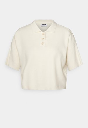 Polo a maniche corte in maglia color crema con tre bottoni e colletto a coste, esposta su uno sfondo bianco semplice.