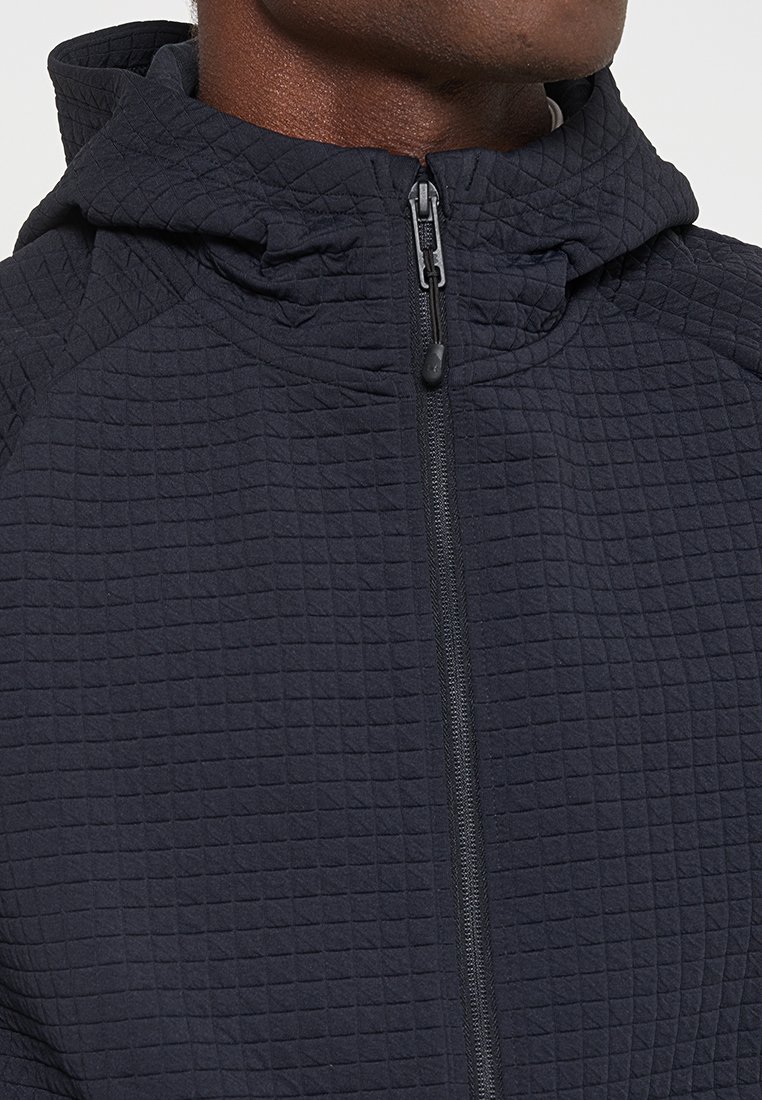 Felpa con zip trapuntata di colore blu scuro, con un motivo testurizzato, che presenta un collo alto e una zip centrale per la chiusura.
