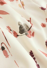 Primer plano de tela color crema con un delicado estampado de flores y hojas abstractas en tonos rosa apagados, granate y gris.