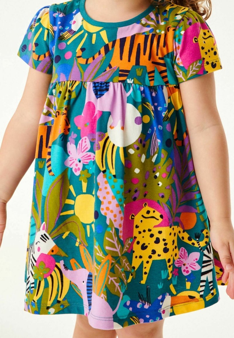 Enfant portant une robe colorée avec des animaux de la jungle, des fleurs, des feuilles et des motifs de soleil dans des tons bleu vif, rose, jaune, vert et orange.