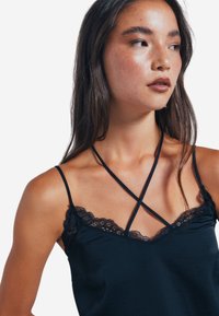 Camisole nera con pizzo lungo il colletto e spalline incrociate. Tessuto liscio con un design aderente che mette in evidenza le spalle.