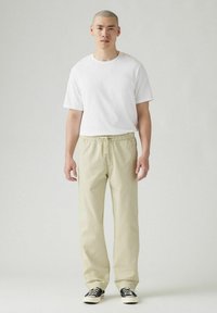 Vit kortärmad t-shirt i kombination med ljusbeige elastiska midjebyxor och svarta sneakers. Simple design med avslappnad passform.