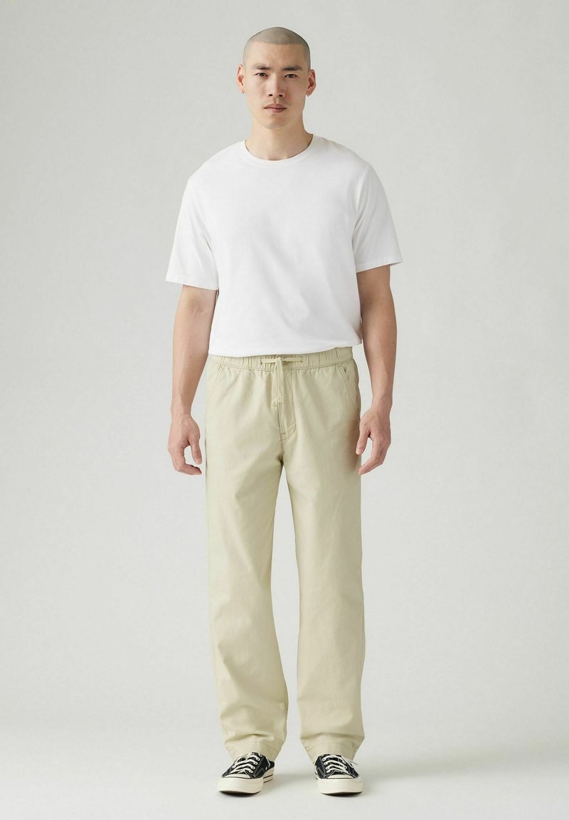 Camiseta blanca de manga corta combinada con pantalones elásticos de cintura clara y zapatillas negras. Diseño sencillo con un corte relajado.