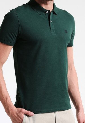 Mørkegrøn polo-shirt med krave, korte ærmer og et diskret logo på brystet. Lavet af glat, letvægtsstof.