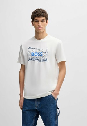 Weißes T-Shirt mit kurzen Ärmeln, das ein blaues "BOSS"-Logo und ein blaues abstraktes Kartenmuster auf der Vorderseite zeigt, kombiniert mit blauen Jeans.