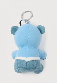Hladký modrý medvídek na klíče z pohledu zezadu, s ušima a kalhotami s denimovou texturou, připevněný na stříbrném kovovém kroužku na klíče.