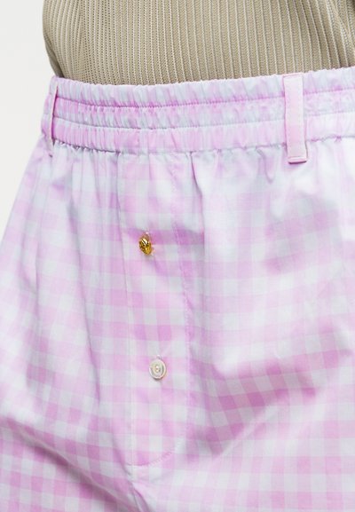 Shorts à taille élastique à carreaux roses clairs et blancs avec deux boutons, un doré et un blanc, présentés sur un mannequin.