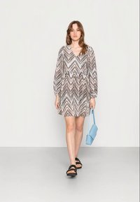 Vestido curto com padrão em chevron em tons de castanho, creme e azul. Apresenta mangas longas, decote em V e um corte solto. Combinado com uma bolsa azul clara.