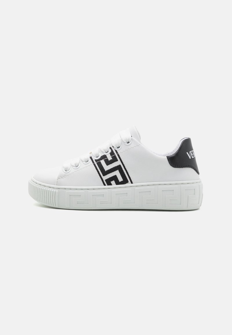 Sneaker blanc avec des accents noirs, présentant une semelle intermédiaire et des lacets à motifs. Design de logo audacieux sur le talon et tige en cuir lisse.