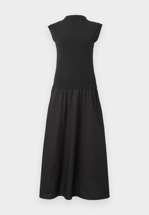 Μαύρο μίντι φόρεμα χωρίς μανίκια με ψηλό στρογγυλό λαιμό και πλισέ φούστα σε σχήμα Α σε απλό φωτεινό φόντο.