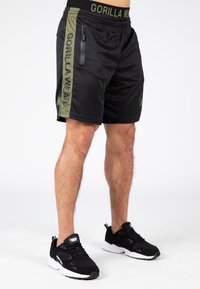 Pantaloni sportivi neri con accenti laterali verdi, dotati di una tasca con zip e branding "GORILLA WEAR" sulla vita e sul lato.