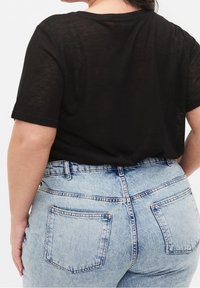 Černý krátký rukáv top vyrobený z lehkého materiálu, spárovaný s džínami světle modré barvy s vysokým pasem, které mají zadní kapsy a mírně vyšisovaný vzhled.