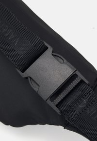 Musta kangasremmi, jossa on teksturoitu pinta, nopea muovinen solki ja kudottu kuvio, suunniteltu kestävyys ja helppokäyttöisyys mielessä.