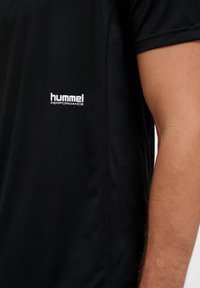Zwarte sport T-shirt van lichte stof met een klein wit "hummel PERFORMANCE" logo aan de linkerkant. Glad van textuur.