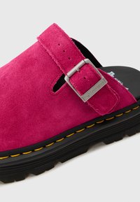Pink suede clog with a strap and silver buckle detail, featuring a black rubber sole accented with yellow stitching.
